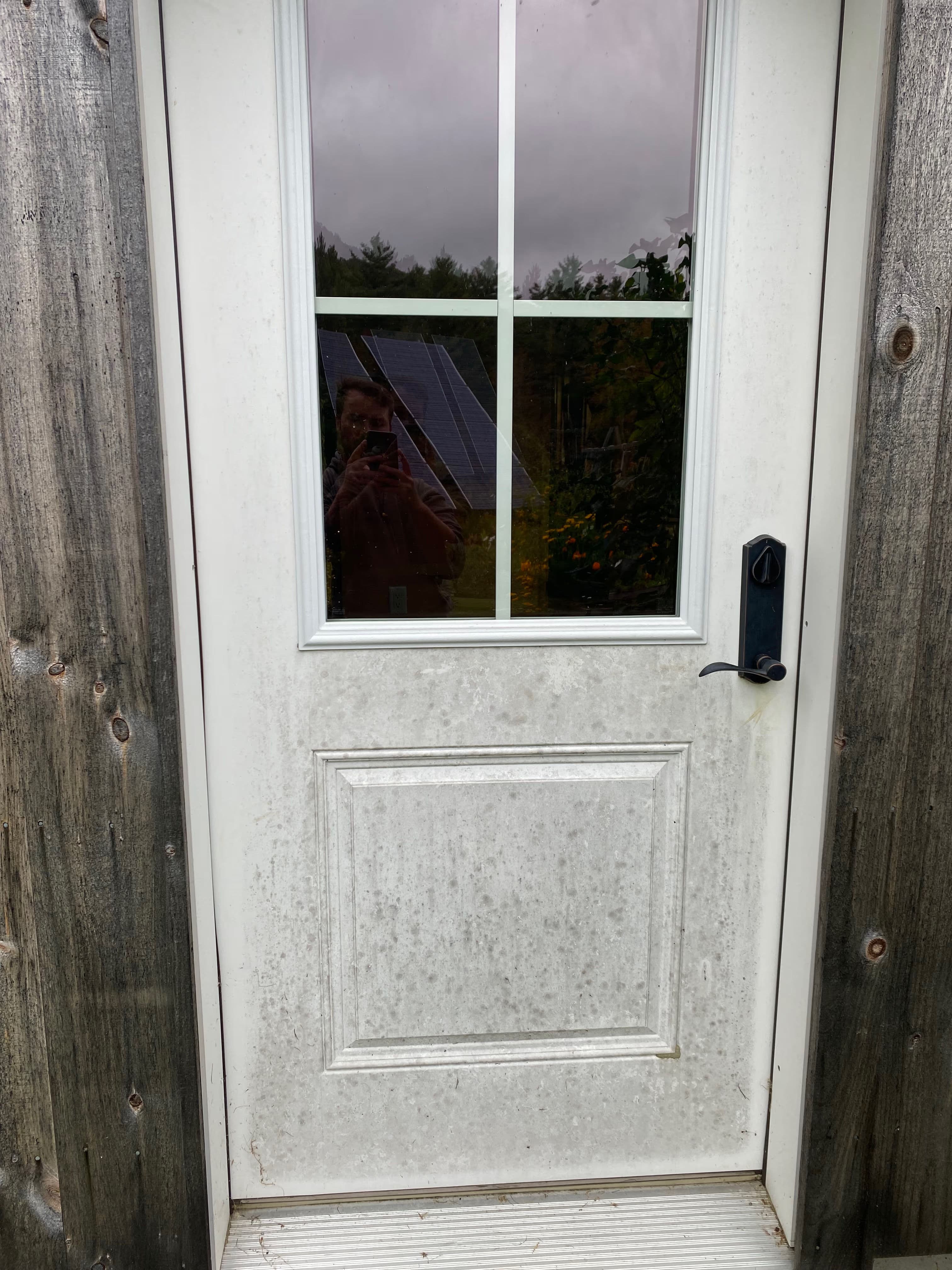 White door with a window, weathered wood frame, reflective surface, and nearby solar panels.