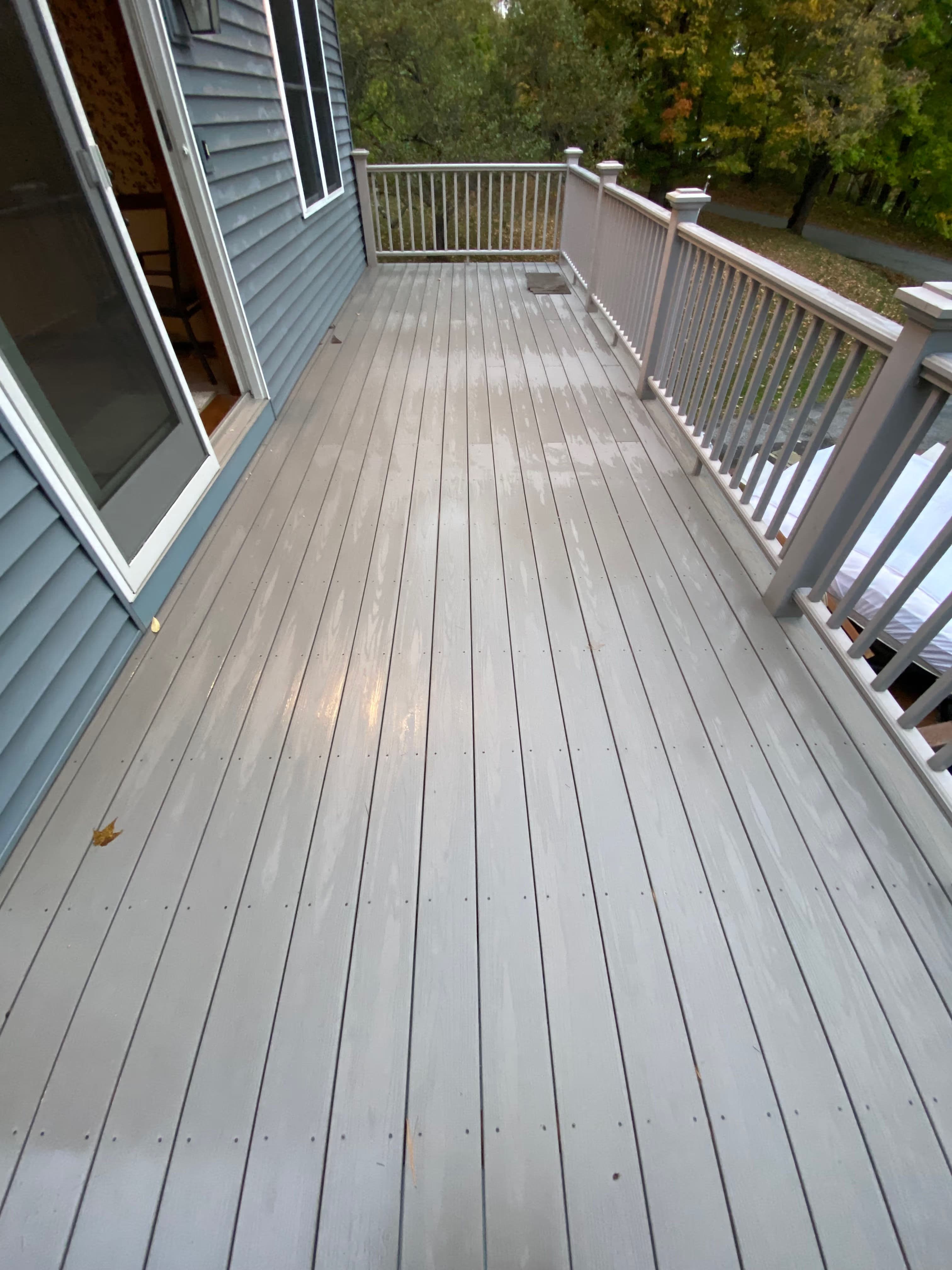 Freshly painted gray deck with wooden railing, surrounded by greenery.