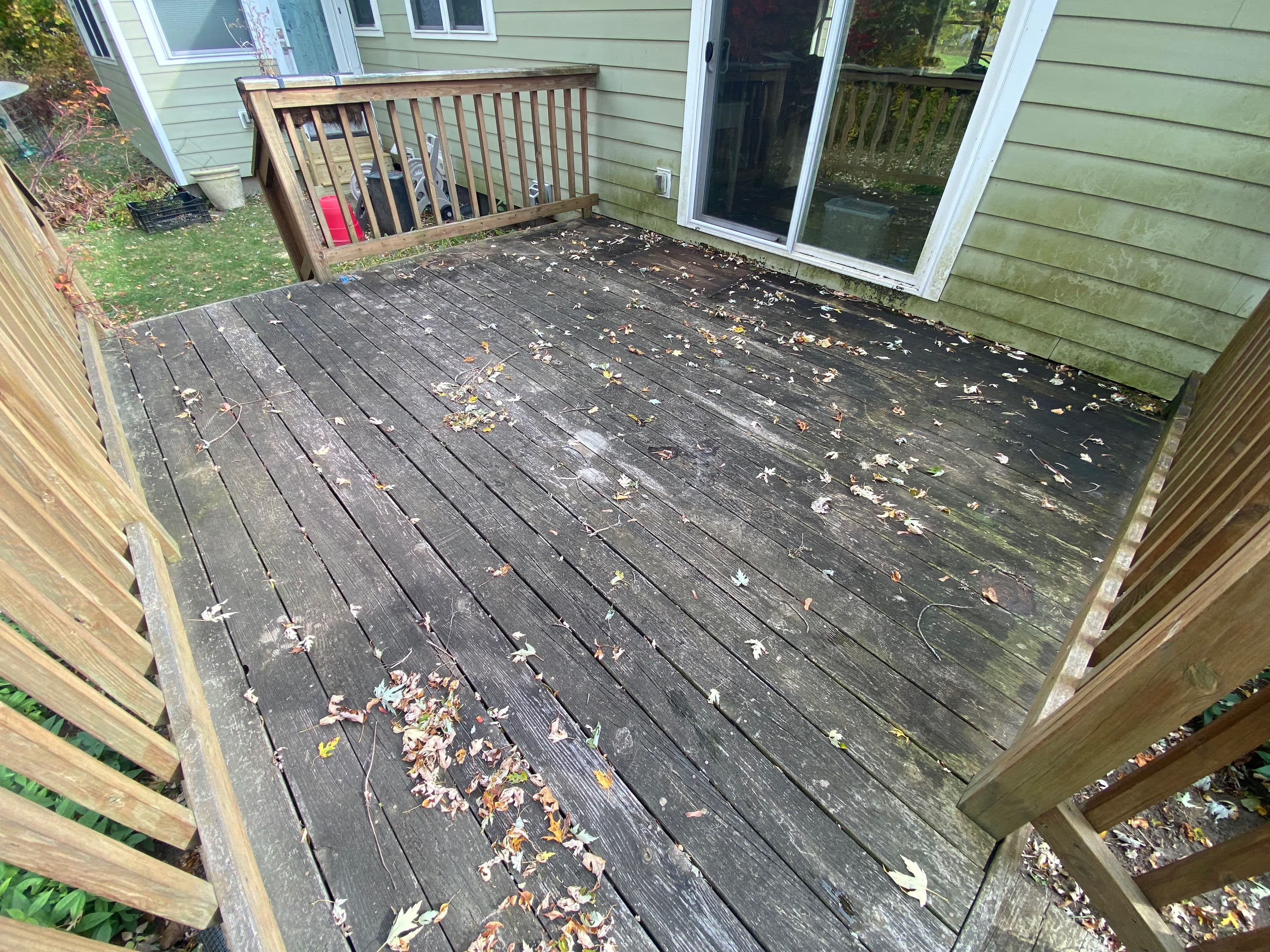 Wooden deck with fallen leaves, showing signs of weathering and wear near a house.