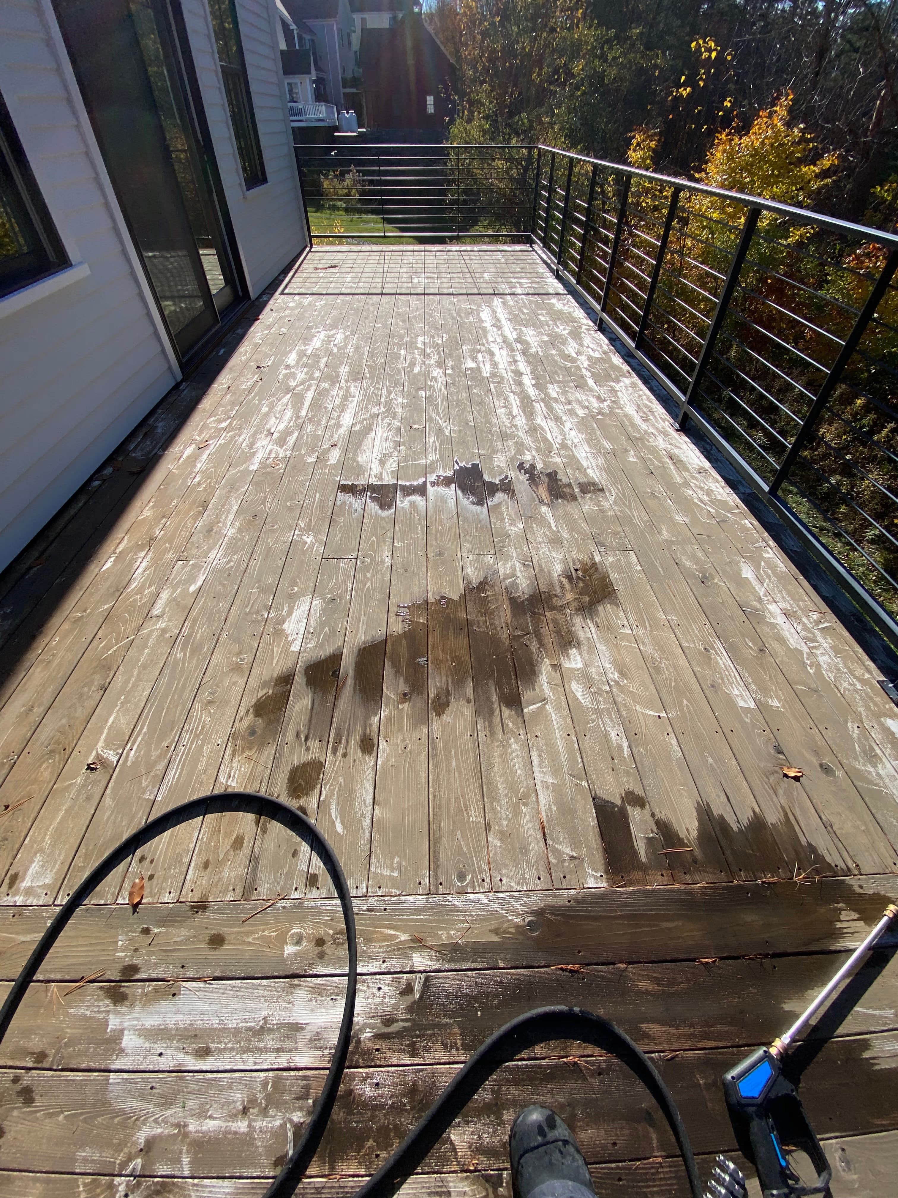 Deck cleaning process showing wet wooden surface and cleaning equipment on a sunny day.