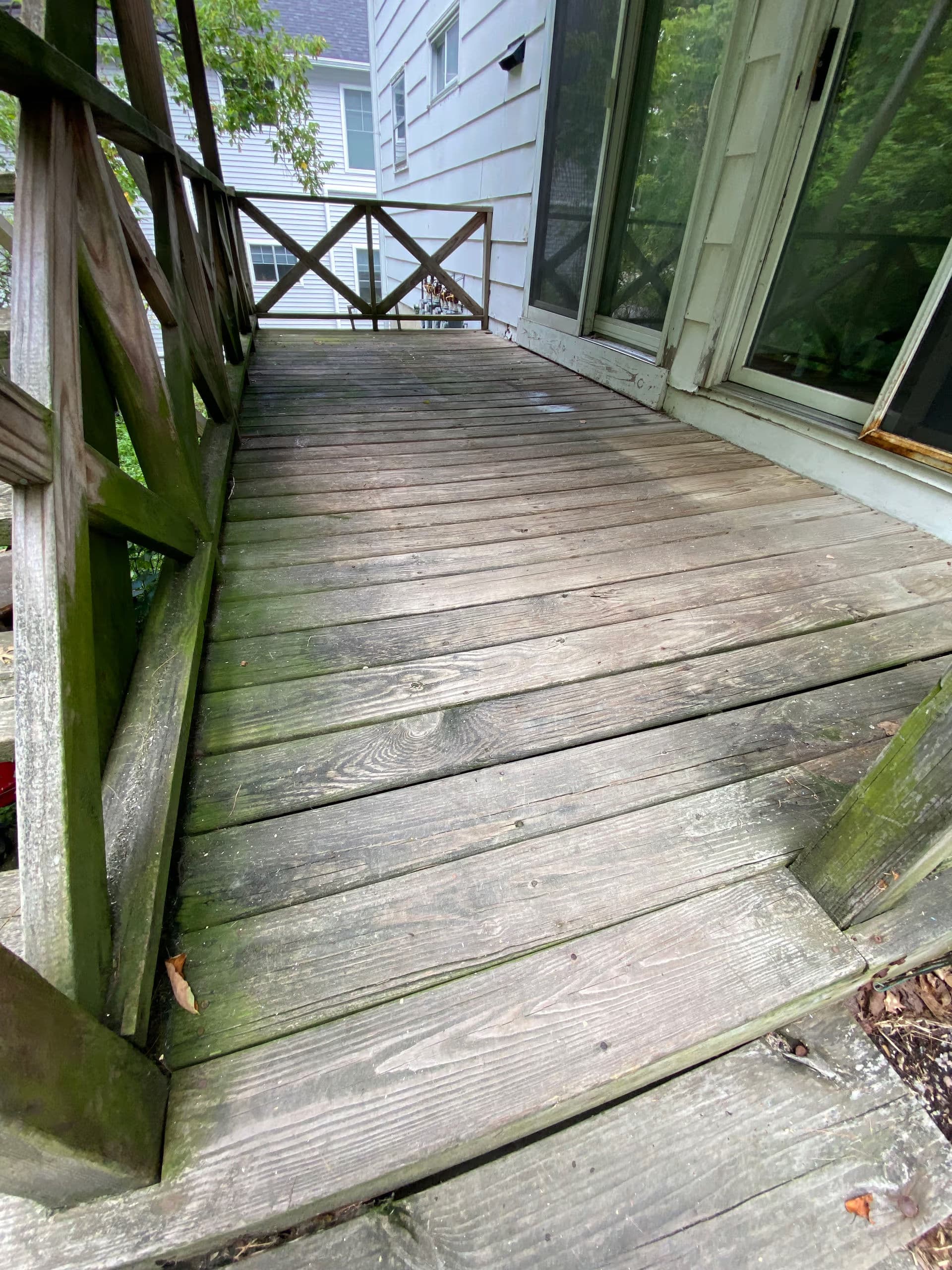 Wooden porch with weathered planks and a railing, surrounded by greenery.