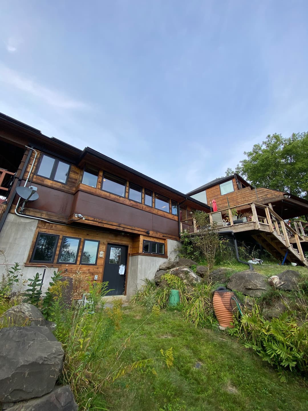 Modern wooden house with outdoor deck and lush greenery in a scenic landscape.