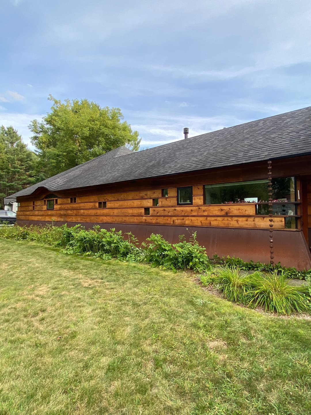 Wooden cabin with a landscaped yard, surrounded by trees under a blue sky.