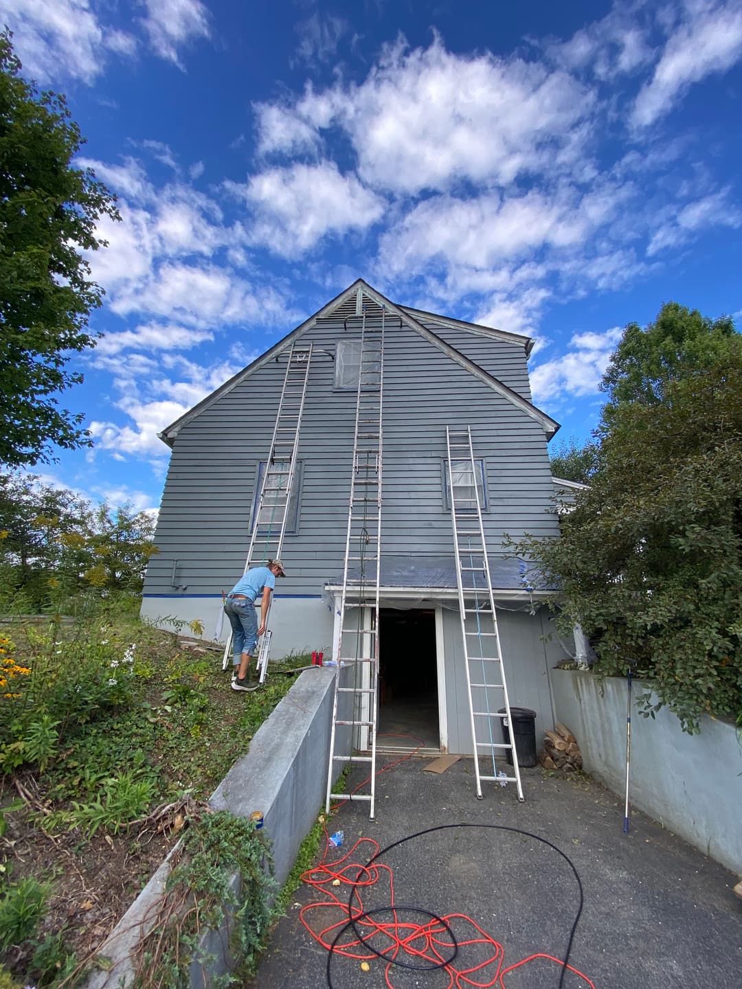 Man painting a house with ladders under a blue sky, showcasing home renovation work.