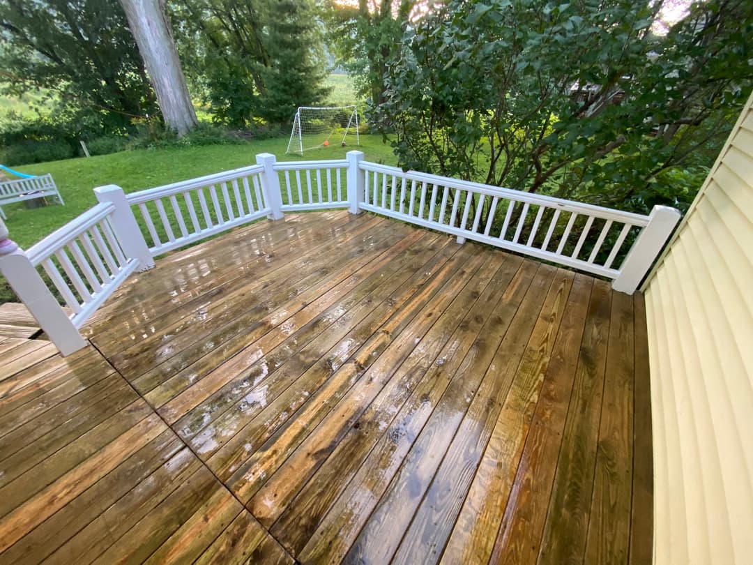 Clean wooden deck with white railing, surrounded by greenery and a soccer goal in the background.
